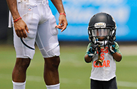 Child standing next to football player, wearing helmet